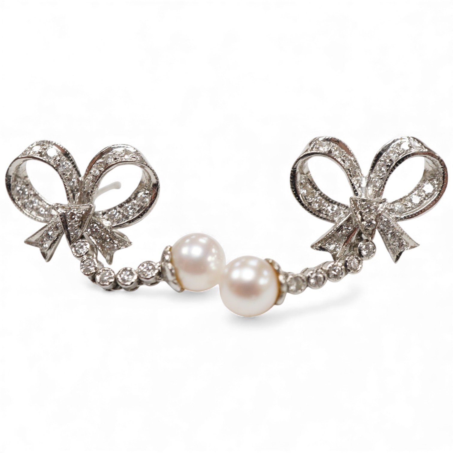 A pair of white metal, single stone cultured pearl and diamond cluster set drop earrings, of ribbon bow design, overall approx. 27mm.